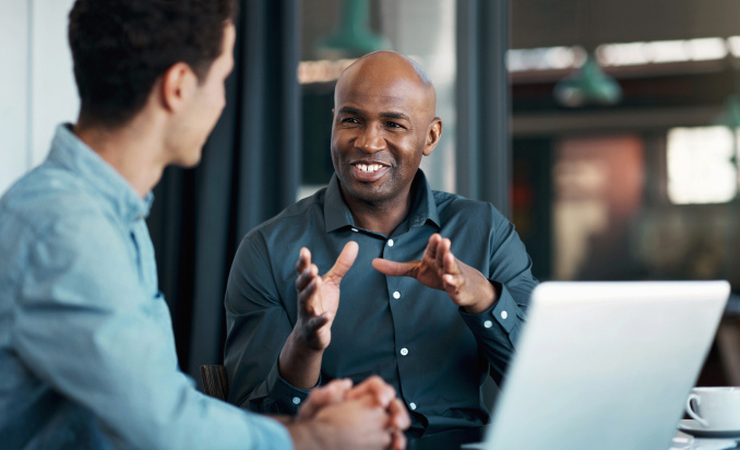 Professional man seated at table explaining a concept to a male colleague.